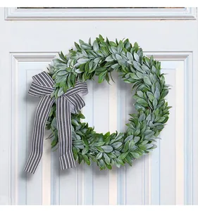Close-up of a lush green leaf wreath with black and white striped bow on white door