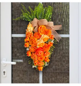 Close-up van een oranje bloemenkrans in de vorm van een wortel aan een witte deur