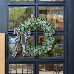 Lush green artificial leaf wreath decorated with a classic black and white striped bow