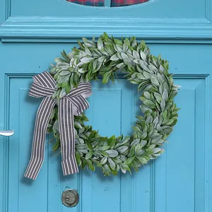 Decorative green lamb's ear wreath with black and white striped bow on blue door.
