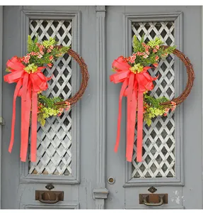 Pair of decorative floral wreaths with large red bows hanging on a grey lattice door
