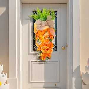 Creatieve paaskrans in de vorm van een wortel met oranje rozen op een witte deur.