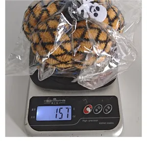 Gestrickte Halloween-Kürbis-Deko wiegt 157g auf einer digitalen Küchenwaage in Folie.