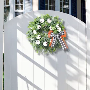 Decoratieve oogstkrans met witte pompoenen en een geruite strik op een witte poort