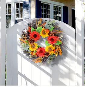 Decorative fall wreath with sunflowers and pinecones hanging on a white wooden gate.