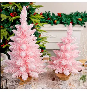 Dettaglio di due alberi di Natale rosa floccati con effetto neve e base in tela juta.