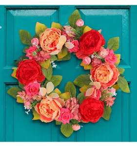 Couronne de pivoines artificielles rouges et roses sur une porte turquoise.