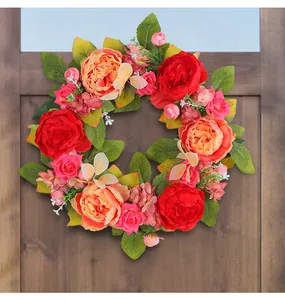 Couronne de pivoines artificielles rouge et rose suspendue à une porte en bois