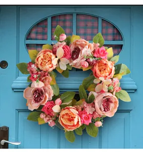 Realistic artificial peony flower wreath hanging on a classic blue door for home decor