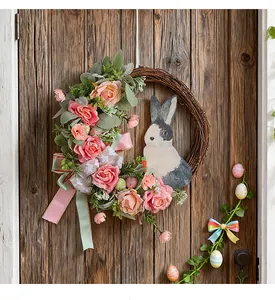 Detailansicht eines Osterkranzes mit rosa Rosen, Hasenfigur und Eiern an einer rustikalen Tür.