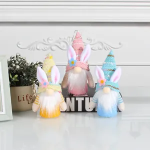 Drei bunte Osterwichtel-Plüschpuppen mit Hasenohren und Strickmützen auf weißem Tisch.