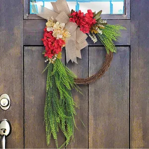 Rustic farmhouse front door wreath with red flowers and a large burlap bow hanging