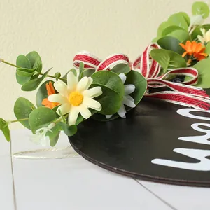 Close-up of artificial daisies and red striped ribbon on wooden door sign