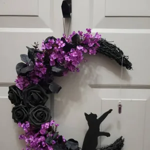 Detail view of a Halloween moon wreath with black roses, purple flowers, and a cat silhouette.