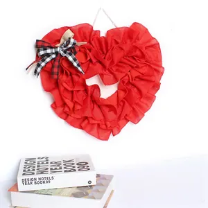Red burlap heart shaped wreath with decorative checkered bow hanging against white wall