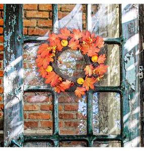 Detail view of a fall maple leaf and pumpkin wreath hanging on a rustic vintage window.