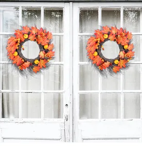 Two autumn wreaths with maple leaves and pumpkins hanging on a rustic white wood window