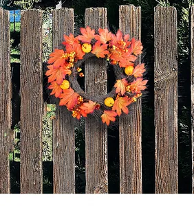 Beautiful autumn harvest wreath with maple leaves and pumpkins hanging on a rustic wooden fence