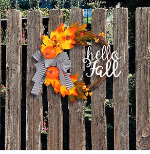 Detail view of an autumn wreath with maple leaves and pumpkins on a rustic wooden fence.