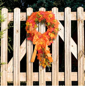 Detailed view of autumn maple leaf wreath with a large orange bow hanging on a fence
