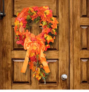 Autumn maple leaf wreath with large orange bow hanging on a rustic wooden door detail.