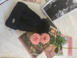 Dettaglio del berretto in maglia nera con pompon di pelliccia e spilla a foglia.