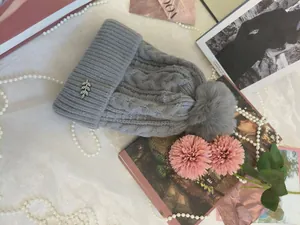 Dettaglio di un berretto invernale grigio a trecce con pompon e spilla a foglia di strass.