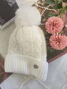 Primo piano di un berretto bianco a trecce con grande pompon e spilla a foglia decorativa
