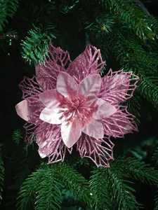 Primer plano de una flor de Navidad rosa con purpurina en una rama de pino verde frondoso.