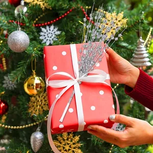 Festliche silberne Glitzerbeeren-Zweige schmücken eine rote Geschenkbox am Baum