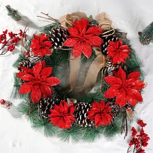 Festive Christmas wreath with red glitter poinsettia flowers and pine cones on a snowy background.