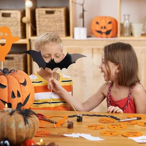 Children crafting Halloween decorations with paper bats and pumpkin stickers at home.