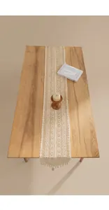 Detail eines cremefarbenen Häkelspitzen-Tischläufers auf einem rustikalen Holztisch.