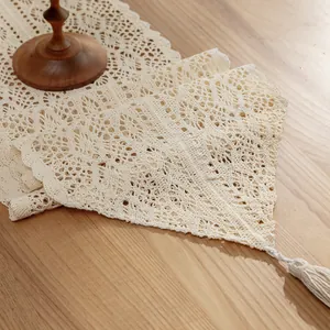 Vintage cream cotton crochet lace table runner with tassels on a light wooden table