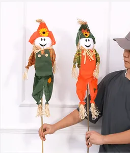 Person holding two Halloween scarecrow decorations with smiley faces and straw hats