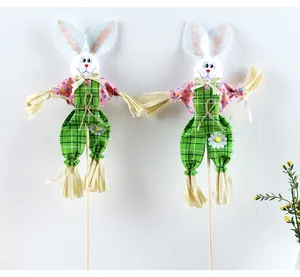 Espantapájaros de conejo de Pascua en pantalones de cuadros verdes en palos largos