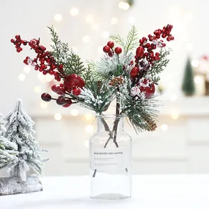 Festive artificial snow pine branches with red berries in glass vase for table decor
