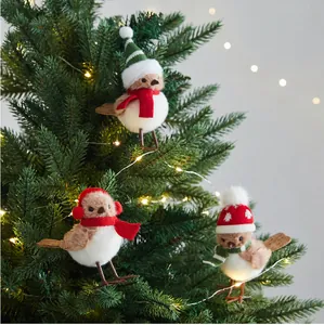 Detail of three cute plush bird ornaments with festive scarves on a lit Christmas tree