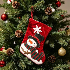 Small red velvet Christmas stocking featuring snowman design hanging on festive tree