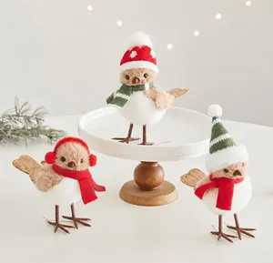 Tre graziose statuine di uccellini natalizi con cappelli e sciarpe su un supporto bianco