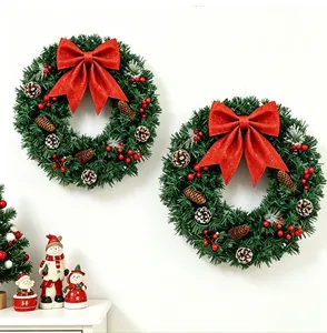 Gros plan de deux couronnes de Noël vertes avec des nœuds rouges sur un mur blanc.