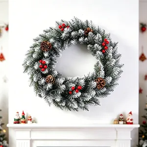 Artificial frosted Christmas wreath with pine cones and red berries on white wall
