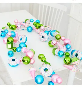 Guirlande de Noël colorée avec beignets et cônes de glace sur une table blanche épurée.