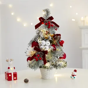 Mini flocked Christmas tree with LED lights and red velvet bow ornaments in a basket