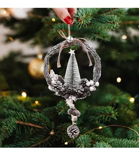 Hand holding a rustic Christmas wreath ornament with pine cones and a mini tree