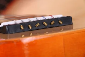 Détail macro du chevalet noir et des chevilles en laiton d'une guitare en bois de 21 pouces