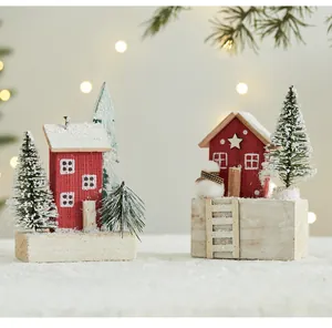 Close-up view of red wooden Christmas house ornaments featuring snowy pine trees and mini snowman