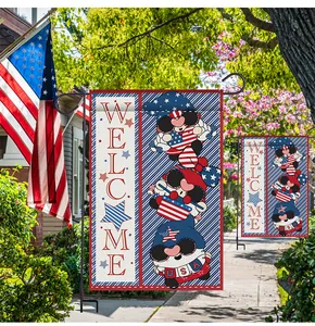 Close-up of Independence Day garden flag with cartoon gnomes and vertical welcome text outdoors.