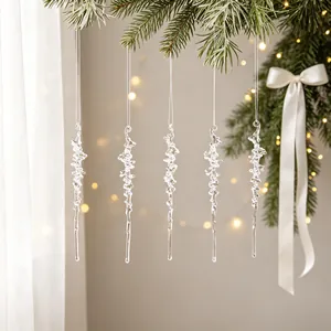 Detailweergave van heldere acryl ijspegelornamenten die aan een besneeuwde kerstboomtak hangen
