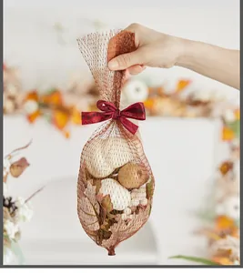 Hand holding mesh bag filled with artificial white pumpkins and fall maple leaves decor